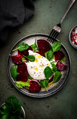 Gourmet salad with burrata cheese, baked beets, spinach and olive oil, green stone background, top view