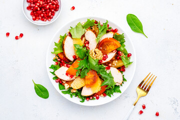 Autumn salad with grilled chicken, persimmon, pomegranate, walnuts, oranges and lettuce, top view