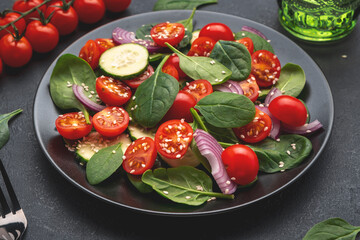 Healthy vegan salad with spinach, tomatoes, cucumber, onion, sesame and olive oil. Black table background, top view