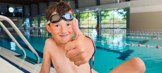 Happy boy giving a thumbs up in an indoor swimming pool. Concept of self-confidence in children's swimming lessons, child development, children's sports