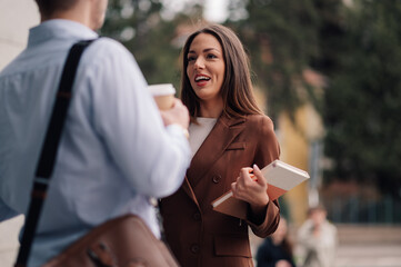 Businesswoman holding notebook talking to businessman drinking coffee outdoors