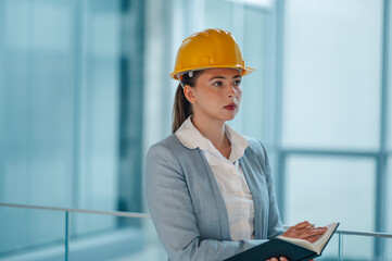 Female engineer wearing hardhat taking notes in modern office building