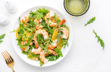 Delicious shrimp salad with juicy orange, fresh arugula and white sesame seeds on white plate, top view