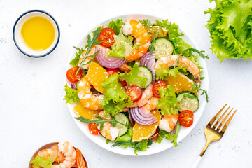 Gourmet seafood salad with big shrimp, orange slices, fresh lettuce, cherry tomatoes, cucumbers, onion and sesame, top view