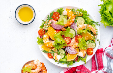 Fresh shrimp salad with orange, lettuce, tomatoes, cucumbers, onions and sesame seeds with olive oil, white background, top view
