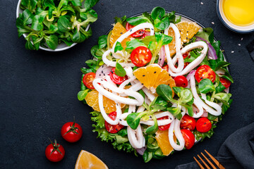 squid salad with oranges, tomatoes, lettuce and lemon dressing, black background, top view