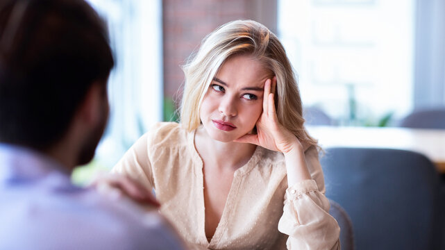 Young Caucasian woman disinterested in blind date, feeling bored with conversation at city cafe. Millennial couple having relationship problems, going through breakup or divorce