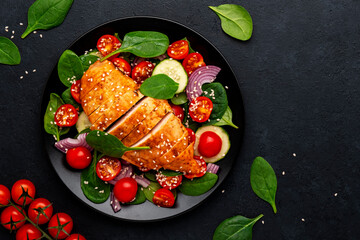 Healthy vegetable salad with grilled chicken, spinach, tomatoes, cucumber and red onion. Black table background, top view