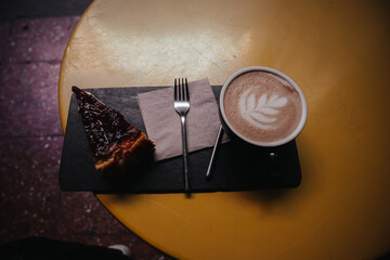 Delicious slice of cake with latte coffee, perfect for enjoying a relaxing moment. A slice of chocolate cake with coffee and latte art on a yellow table setting, perfect for a relaxing cafe experience