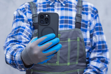 Close-up of a construction worker handyman in protective gloves and workwear using a modern...