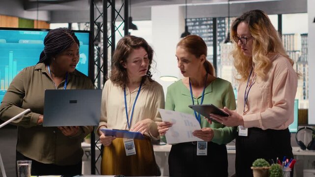 Multiethnic women form a powerful team discuss business strategy, analyzing performance data on laptop and documents aligned around success, progress and shared objectives. Camera B.