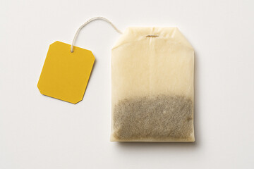 Close up shot of a tea bag with a yellow tag on a white surface in a studio setting plain background