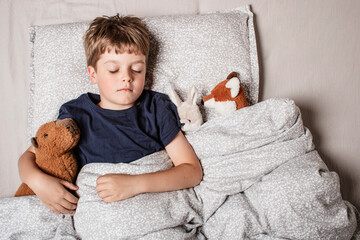 Cute little boy sleeping peacefully in bed, holding soft stuffed animals. Cozy childhood bedtime...
