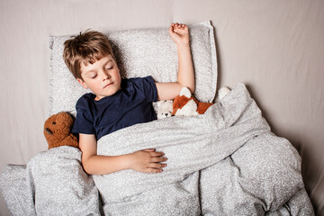 Cute little boy sleeping peacefully in bed, holding soft stuffed animals. Cozy childhood bedtime...