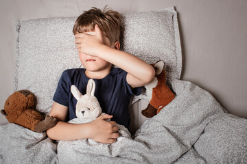 The boy was scared before going to bed. Night terrors in a child. The kid covers his face with his...