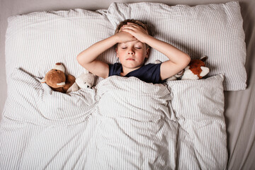 Cute little boy sleeping peacefully in bed, holding soft stuffed animals. Cozy childhood bedtime...