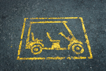 A distinct yellow painted symbol of a golf cart is clearly visible on a dark, textured asphalt surface. The white rectangular outline contains the stylized golf cart icon.