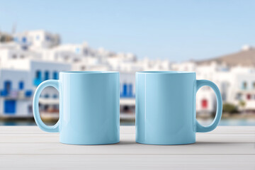 Two pastel blue mugs mockup on a wooden table with a scenic view of white buildings in a Greek island