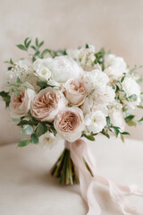 Delicate wedding bouquet in soft neutral tones with peonies and garden roses, tied with a flowing ribbon