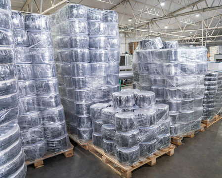 Stacks of plastic spools packed in stretch film on wooden pallets in modern warehouse. Industrial packaging, logistics and plastic product manufacturing.