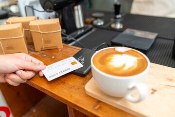 Small business entrepreneur barista coffee shop cafe restaurant. Customer tap credit card on card swipe machine making online banking payment buy coffee at cashier counter. Cashless payment technology