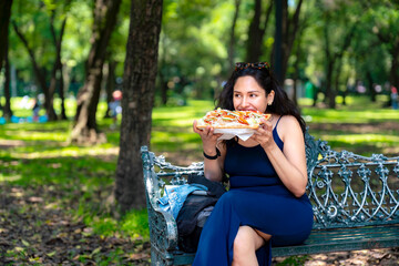 A happy young Latina woman in a navy blue dress sits casually on a bench in Chapultepec, enjoying a...