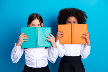Two adorable schoolgirls in white uniforms holding colorful book with cheerful expressions