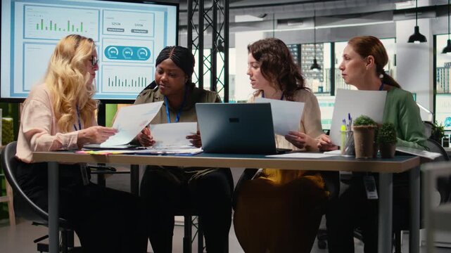 Group of businesswomen engaging in collaboration during briefing session, analyzing data and writing reports while embracing a mindset of growth. Goals oriented meeting. Camera A.