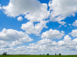 Blue sky with fluffy white cumulus clouds over a green field, perfect weather scene for...