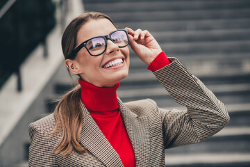 Confident businesswoman outdoors wearing glasses and elegant jacket, smiling happily on urban...