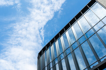 Contemporary office building with reflective glass windows and clear blue sky with scattered clouds. Suitable for illustrating architecture, business, or urban development concepts.