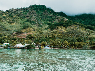 Tropical shoreline homes below lush green mountains on Moorea Island, Tahiti.