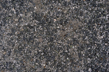 Rough, uneven gravel stones in various shades of gray and black cover the entire frame. Suitable for backgrounds, construction, landscaping, or texture design projects.