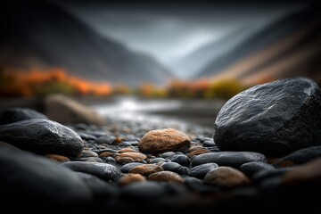 A tranquil river scene featuring smooth, dark stones in the foreground with a blurred background of mountains and autumn foliage.