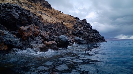 Obraz premium Waves crash against a rocky, grassy coastline under clouds.