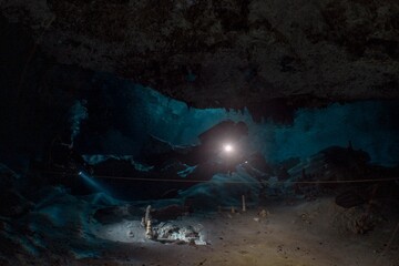 A diver explores a dark, underwater cave with a bright spotlight.