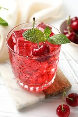 Tasty cherry soda with ice cubes, berries and mint in glass on white wooden table, closeup