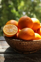 Fresh whole and cut oranges in wicker basket on wooden table against blurred green background, closeup