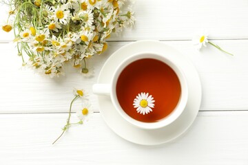 Aromatic tea in cup and chamomile flowers on white wooden table, flat lay