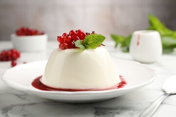 Delicious panna cotta with red currants, sauce and mint on white marble table against blurred background, closeup