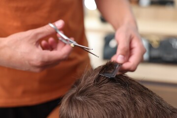Professional barber cutting boy's hair in barbershop, closeup