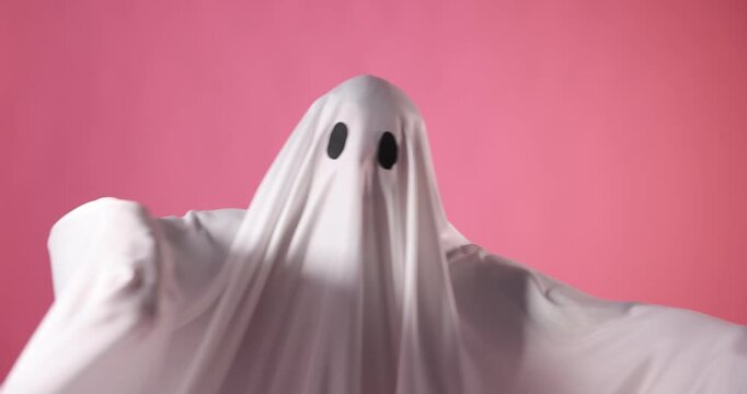 Creepy ghost. Man covered with white sheet showing scary moves on pink background