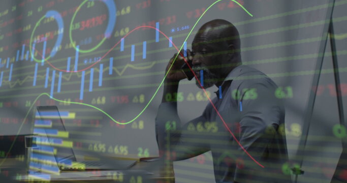 Speaking man wearing shirt at office desk, holding smartphone with laptop data overlay, copy space
