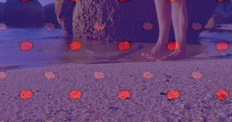 Standing male legs and bare feet dipping in pebbly beach water, with mossy rock, red starbursts