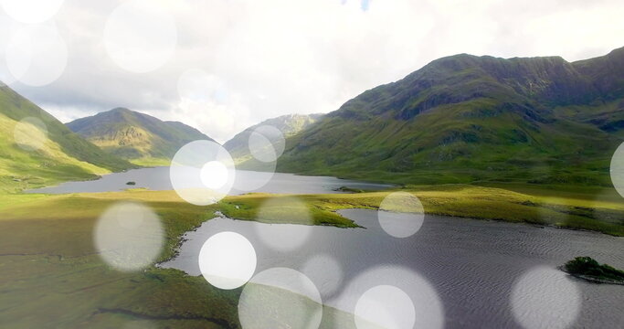 Fototapeta Shimmering mountain lake reflecting sunlight in remote valley, with green hills, light artifacts