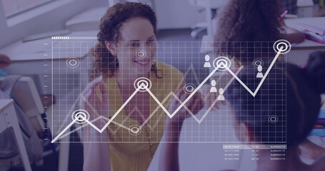 Gesturing teacher wearing yellow blouse teaching kids in classroom, with laptops and graph overlay
