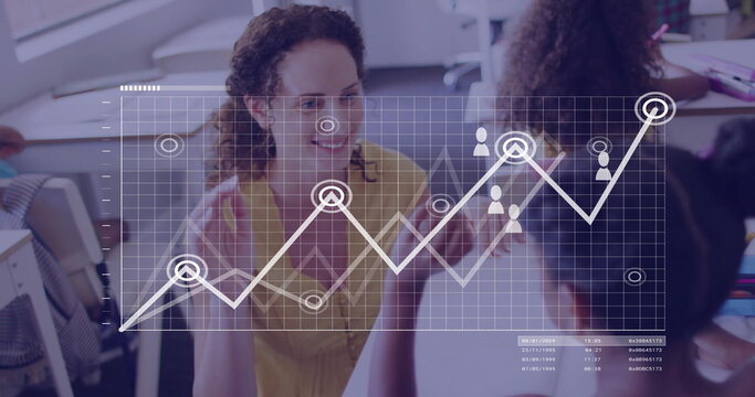 Gesturing teacher wearing yellow blouse teaching kids in classroom, with laptops and graph overlay