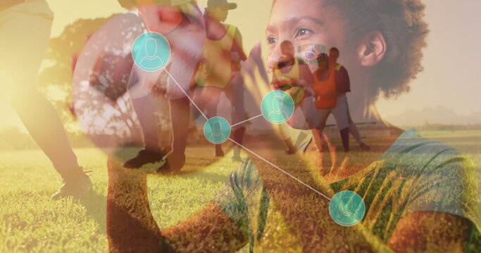 Reaching teen girl tapping network nodes at soccer field with orange-bibbed teammates passing ball