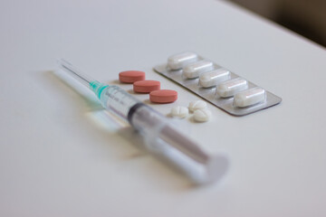 Syringe, pills and capsules resting on white table
