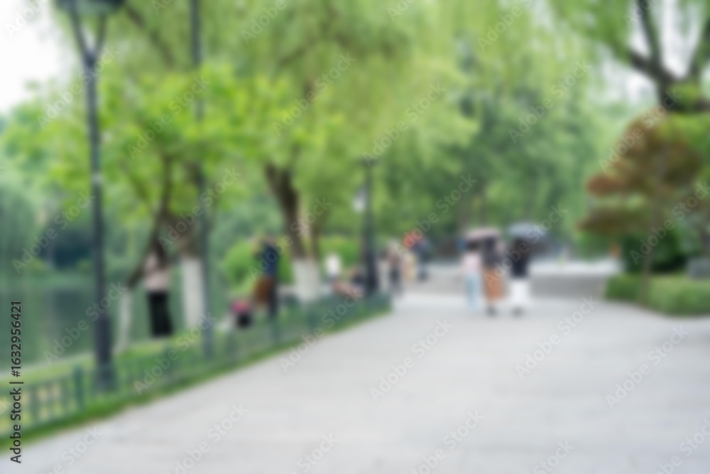 Poster a blurred image of a pathway in a park with trees and people walking by.